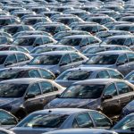 Αυξημένοι δασμοί στα κινεζικά EV; Rows of a new cars parked in a distribution center on a car factory on a sunny day. Top view to the parking in the open air
