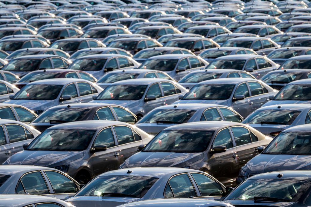 Rows of a new cars parked in a distribution center on a car factory on a sunny day. Top view to the parking in the open air